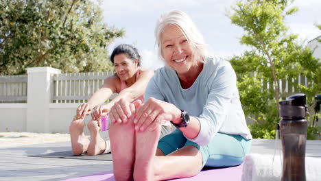 Two-happy-diverse-senior-women-stretching-and-smiling-in-sunny-garden,-slow-motion