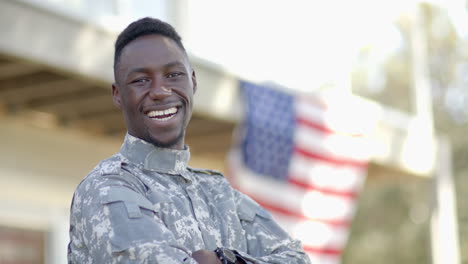 Glücklicher-Afroamerikanischer-Soldat,-Der-An-Einem-Sonnigen-Tag-Mit-Der-Flagge-Im-Hintergrund-Lacht,-Zeitlupe