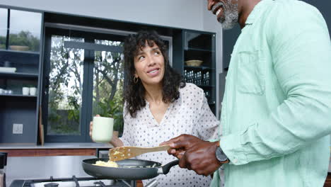 Happy-biracial-couple-cooking-and-preparing-scrambled-eggs-on-pan-in-kitchen,-slow-motion