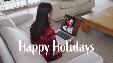 Animation-of-happy-holidays-text-over-caucasian-woman-on-laptop-screen-and-christmas-decorations