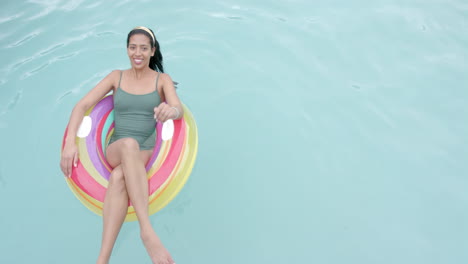 Young-biracial-woman-enjoys-a-swim-on-a-colorful-float,-with-copy-space