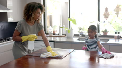 Happy-biracial-mother-and-daughter-cleaning-kitchen-worktop-together,-slow-motion