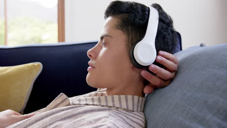 Happy-biracial-man-in-headphones-lying-on-couch-with-eyes-closed,-slow-motion
