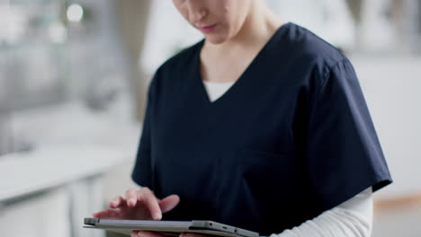 Portrait-of-happy-caucasian-female-doctor-wearing-scrubs-using-tablet-in-hospital,-slow-motion