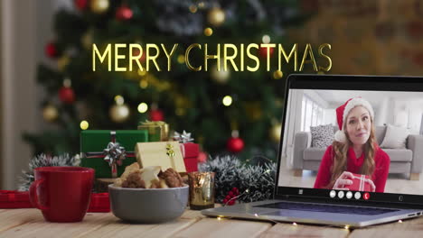 Animation-of-merry-christmas-text-over-caucasian-woman-on-laptop-screen-and-christmas-decorations