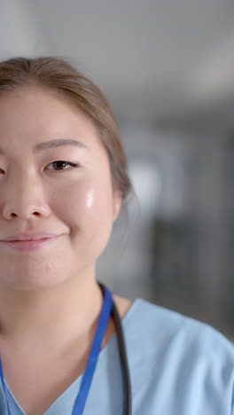 Vertical-video-of-portrait-of-happy-asian-female-doctor-in-hospital-corridor,-slow-motion