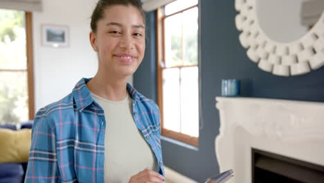 Portrait-of-happy-biracial-teenage-girl-standing-using-tablet-at-home,-copy-space,-slow-motion