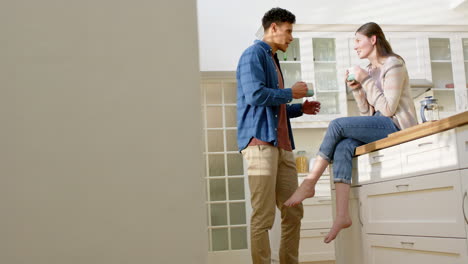 Happy-diverse-couple-talking-and-drinking-coffee-in-kitchen-at-home,-copy-space,-in-slow-motion