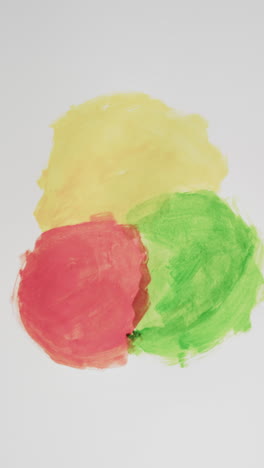 Vertical-video-of-red,-yellow-and-green-powders-with-copy-space-on-white-background