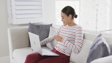 Happy-biracial-woman-sitting-on-sofa-using-laptop-for-online-shopping,-slow-motion