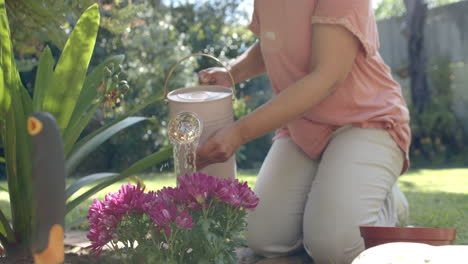 Senior-biracial-woman-watering-flowers-in-sunny-garden-at-home,-slow-motion
