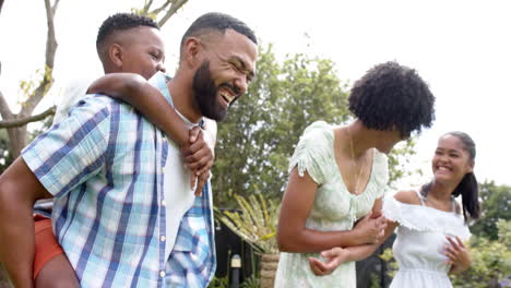 Felices-Padres-Afroamericanos,-Hija-E-Hijo-A-Cuestas-Y-Caminando-En-El-Jardín,-Cámara-Lenta