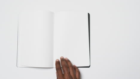 Video-of-hand-of-african-american-man-holding-book-with-blank-page,-copy-space-on-white-background