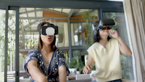 Happy-asian-female-friends-using-vr-glasses-and-dancing-in-sunny-living-room,-slow-motion