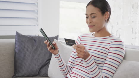 Happy-biracial-woman-sitting-on-sofa-using-smartphone-for-online-shopping,-slow-motion