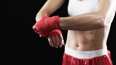 Junge-Kaukasische-Boxerin-Umwickelt-Ihre-Hände-Mit-Roten-Boxbandagen-Auf-Schwarzem-Hintergrund
