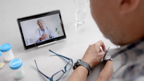 Senior-biracial-male-doctor-and-patient-at-home-having-video-call-on-tablet,-slow-motion