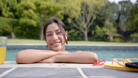 Portrait-of-happy-biracial-teenage-girl-standing-in-sunny-swimming-pool,-slow-motion
