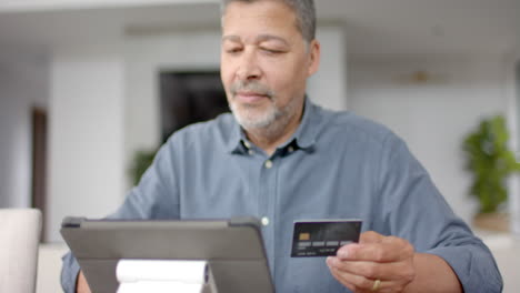 Happy-senior-biracial-man-using-credit-card-and-tablet-for-online-payment,-slow-motion