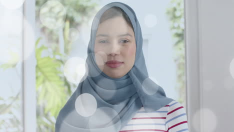 Animation-Von-Lichtpunkten-über-Einer-Gemischtrassigen-Frau-Im-Hijab,-Die-In-Die-Kamera-Blickt