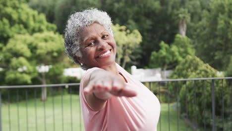 Happy-senior-african-american-woman-practicing-yoga-smiling-on-balcony,-slow-motion