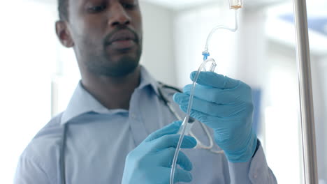 Focused-african-american-male-doctor-in-gloves-injecting-drip-of-patient-with-syringe,-slow-motion