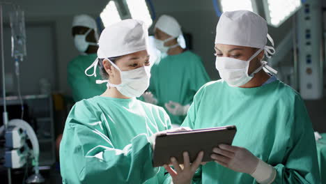 Diverse-female-surgeons-using-tablet-in-operating-theatre-at-hospital,-slow-motion