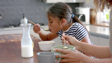 Madre-Birracial-E-Hija-Comiendo-Cereales-Para-El-Desayuno-En-Una-Cocina-Soleada,-Cámara-Lenta