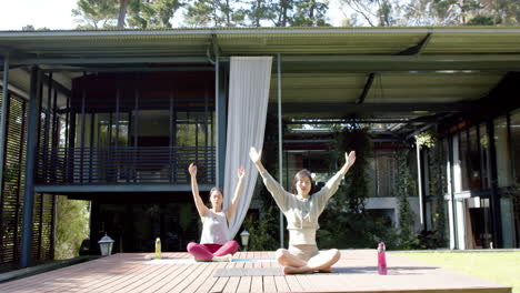 Amigas-Asiáticas-Enfocadas-Practicando-Meditación-De-Yoga-En-Una-Terraza-Soleada,-Cámara-Lenta