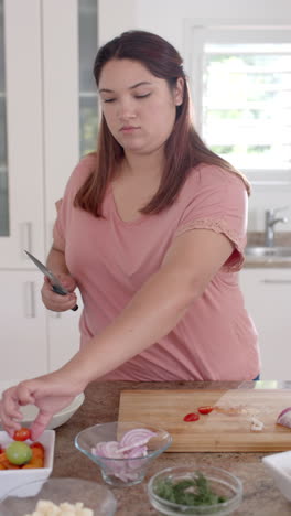 Vertical-video-of-plus-size-biracial-woman-preparing-healthy-salad-in-kitchen,-slow-motion