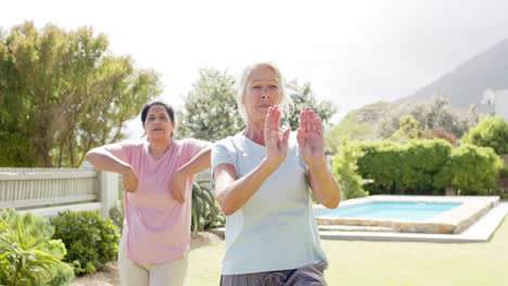 Zwei-Konzentrierte,-Vielfältige-ältere-Frauen-Praktizieren-Yoga-Im-Sonnigen-Garten,-Zeitlupe,-Kopierraum