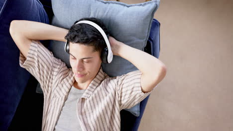 High-angle-of-happy-biracial-man-in-headphones-lying-on-couch-with-eyes-closed,-slow-motion