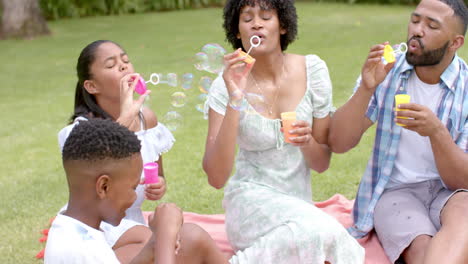 Glückliche-Afroamerikanische-Eltern,-Tochter-Und-Sohn-Pusten-Seifenblasen-Im-Garten,-Zeitlupe