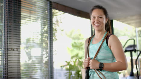 Happy-asian-woman-with-skipping-rope-on-neck-smiling-in-sunny-home-gym,-slow-motion