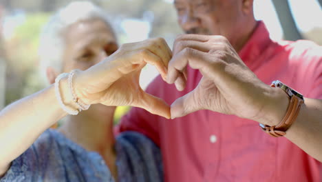 Portrait-of-happy-senior-biracial-couple-making-heart-gesture-in-sunny-garden-at-home,-slow-motion