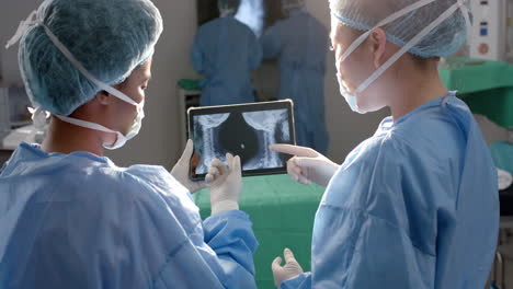 Verschiedene-Chirurginnen-Betrachten-Röntgenaufnahmen-Auf-Einem-Tablet-Im-Operationssaal,-Zeitlupe