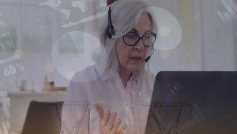 Animation-of-financial-data-processing-over-senior-caucasian-woman-using-phone-headset-and-laptop