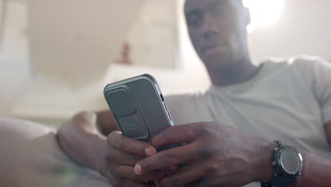 Glücklicher-Afroamerikanischer-Soldat,-Der-Sein-Smartphone-Benutzt-Und-Im-Sonnigen-Wohnzimmer-Lacht,-Zeitlupe