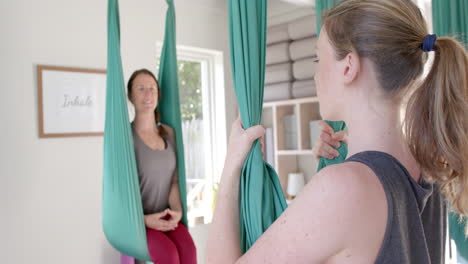 Diverse-fitness-women-exercising-in-aerial-yoga-class-in-big-white-room,-slow-motion