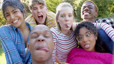 Happy-diverse-group-of-teenage-friends-sitting-on-grass-and-embracing-in-sunny-park,-slow-motion
