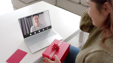 Caucasian-woman-holding-red-gift-using-laptop-with-biracial-man-on-screen