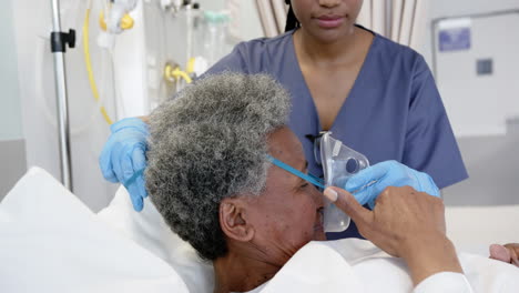 African-american-female-doctor-applying-oxygen-mask-to-senior-woman-in-hospital-room,-slow-motion