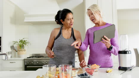 Zwei-Glückliche,-Vielfältige-Seniorinnen,-Die-In-Der-Küche-Mit-Einem-Tablet-Obst-Zubereiten,-Zeitlupe