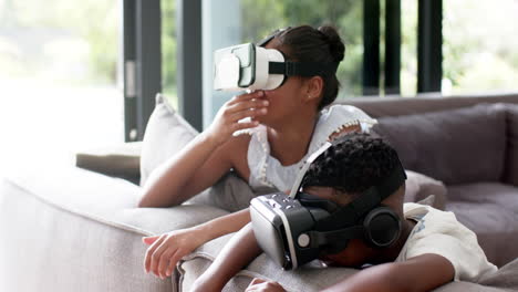 Happy-african-american-brother-and-sister-in-vr-headsets-on-sofa,-slow-motion