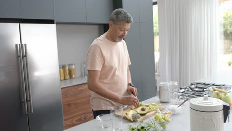 Glücklicher-älterer-Mann-Mit-Gemischter-Abstammung,-Der-In-Der-Küche-Zu-Hause-Zutaten-Für-Einen-Gesunden-Smoothie-Zubereitet,-Zeitlupe