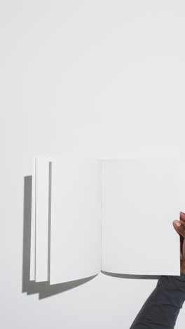 Vertical-video-of-hand-of-african-american-man-with-book-with-white-blank-pages-on-white-background
