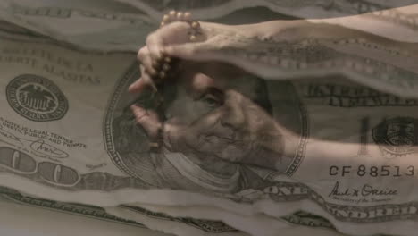 Animation-Von-US-Banknoten-über-Händen,-Die-Einen-Rosenkranz-Halten