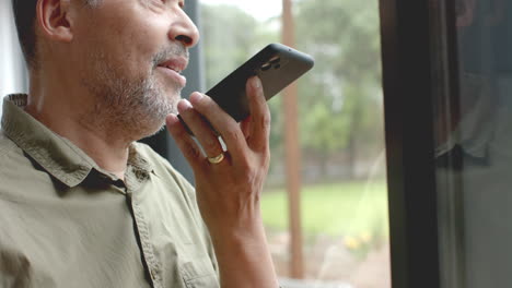 Happy-senior-biracial-man-talking-on-smartphone-standing-by-window-at-home,-slow-motion