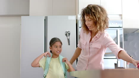 Happy-biracial-mother-and-daughter-prepared-for-school-embracing-in-kitchen,-copy-space,-slow-motion