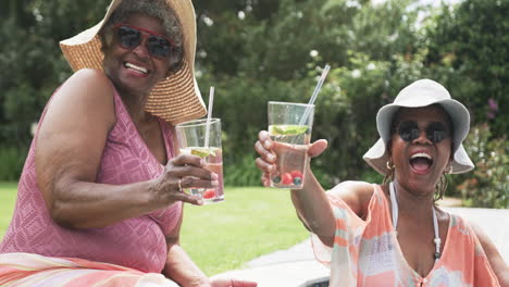 Portrait-of-senior-african-american-female-friends-in-sunhats-making-a-toast-in-garden,-slow-motion